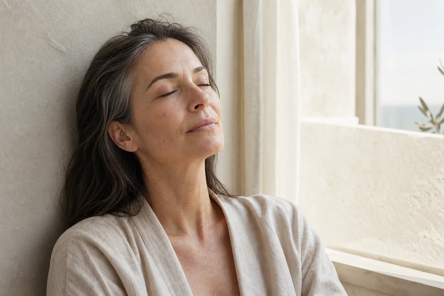 A woman standing in soft early morning light with bare, naturally textured skin
